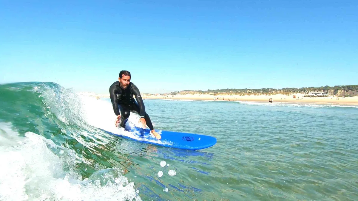 Beginner surfers carrying boards below the fossil cliffs of Costa da Caparica on a half-day trip from Lisbon, Portugal